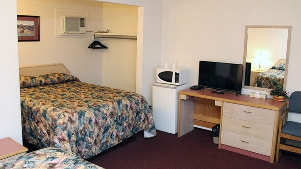 A compact hotel room with a bed, a desk with a television, a small refrigerator, and a mirror. - Silver Star Motel (Vernon)