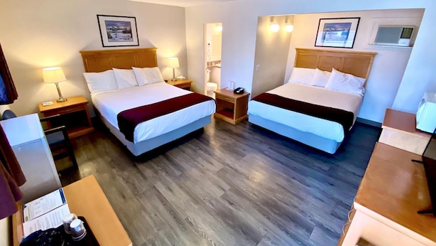 Habitación de hotel con dos camas, suelo de madera, mesitas de noche con lámparas y cuadros en las paredes.