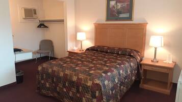 A hotel room with a large bed, two bedside tables with lamps, a chair, a desk with a computer, a microwave, and a painting on the wall.