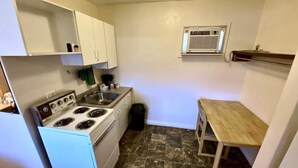 Una cocina pequeña con gabinetes blancos, estufa, lavamanos y una mesita.