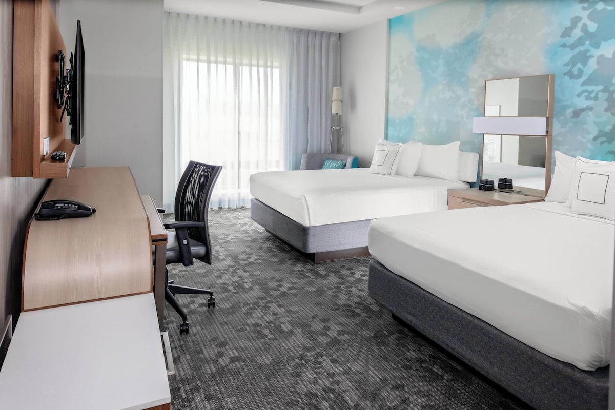 A hotel room with two beds, a desk, a chair, a TV, and a large mirror.