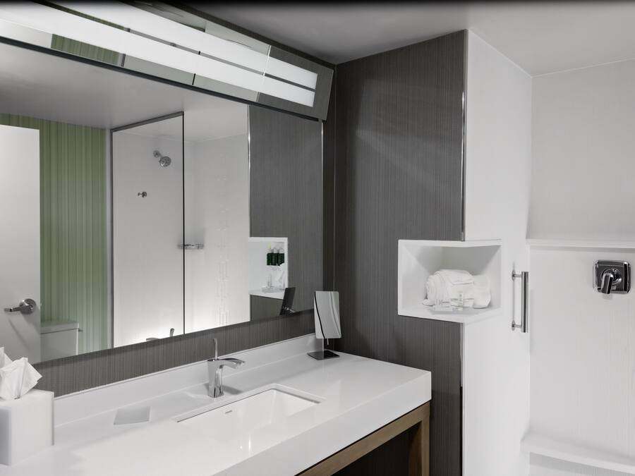 A modern bathroom with a large mirror, white sink, and a towel rack.