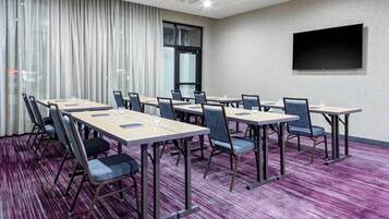 A conference room with multiple tables and chairs, a large window with curtains, and a flat-screen TV mounted on the wall.