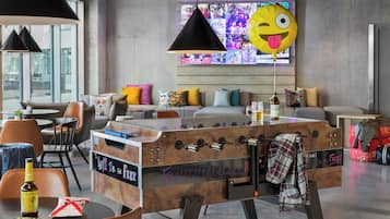 A modern lounge area with a foosball table, comfortable seating, and a large window with a colorful mural.