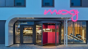 En modern byggnad med en böjd entré och en neonskylt som visar ordet ”mozy”.