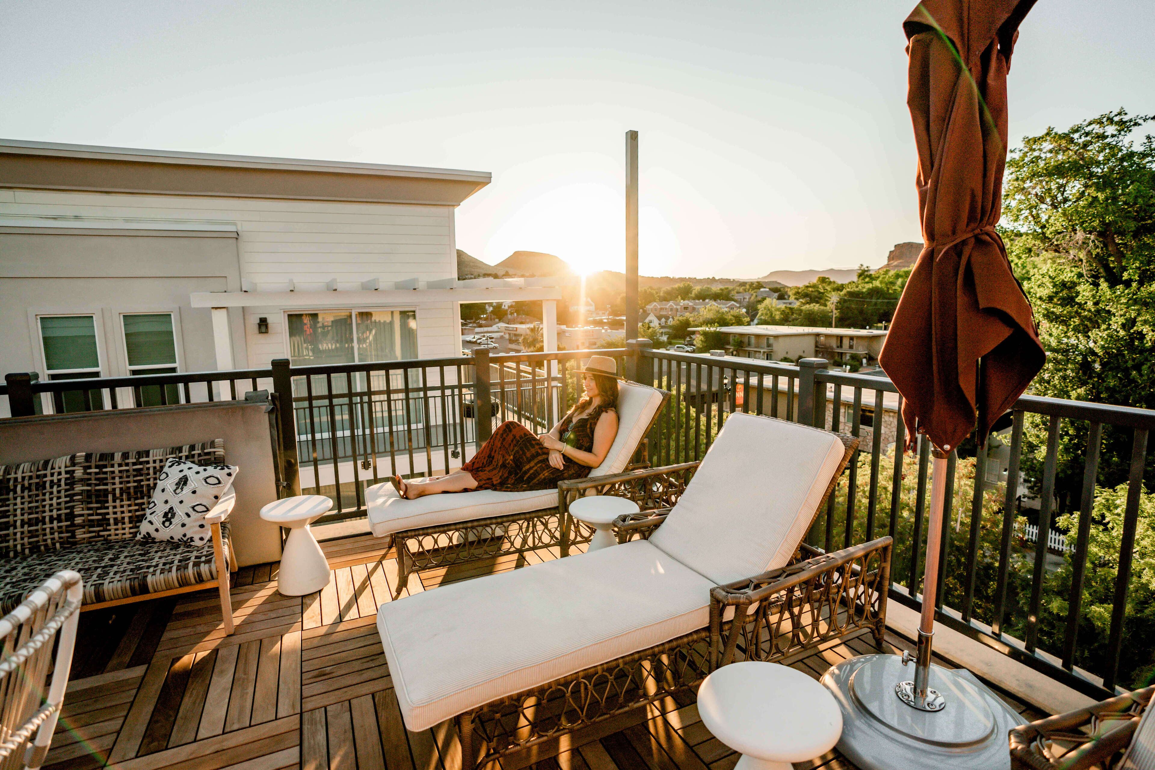 A balcony with wicker furniture, a white building in the background, and a sunset.