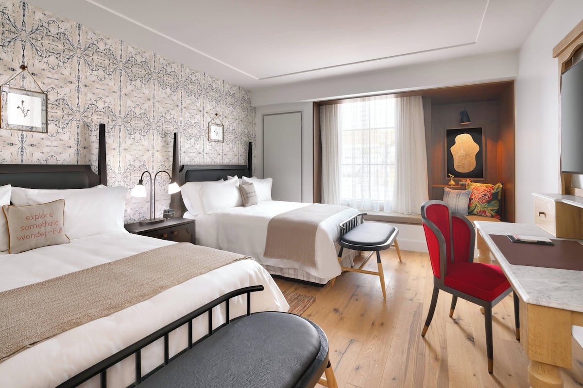 Ein Hotelzimmer mit zwei Betten, einem Schreibtisch, einem Stuhl und einem großen Fenster.