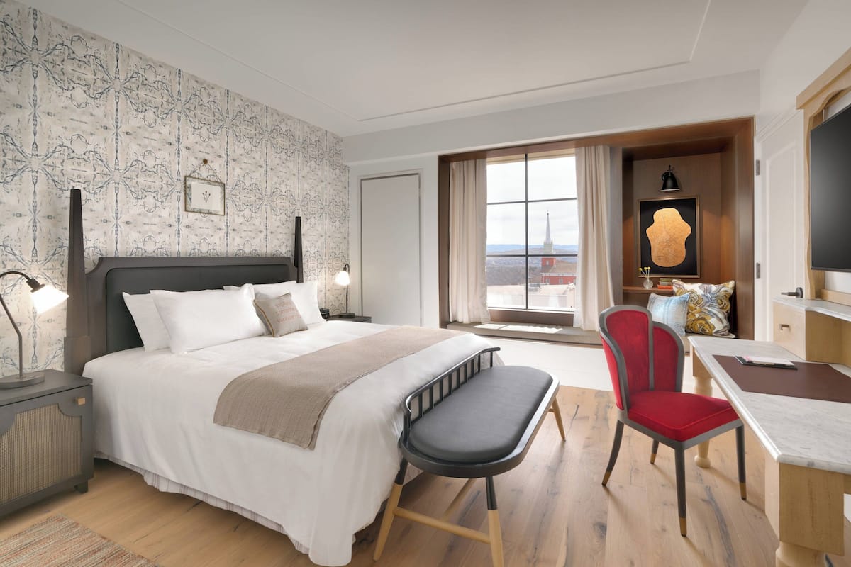 Ein Hotelzimmer mit einem großen Bett, einem Schreibtisch, einem Sessel und Blick auf die Stadt.