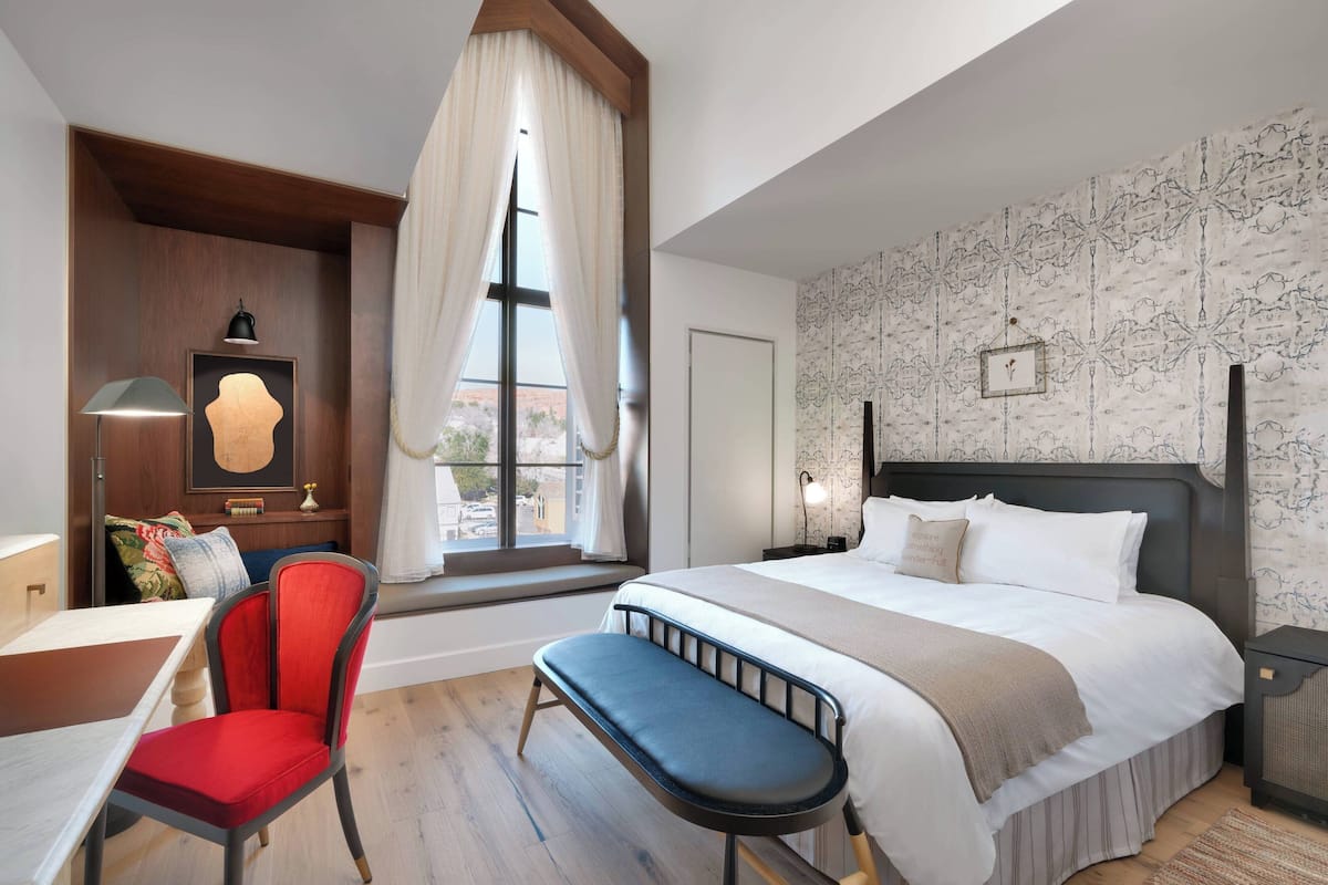 Ein modernes Hotelzimmer mit einem großen Bett, einem Schreibtisch, einem Stuhl und einem Fenster mit Vorhängen.