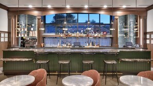 A bar area with a green bar counter, multiple stools, and a seating area with round tables.
