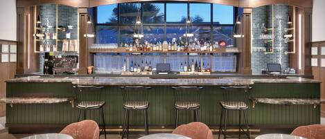 A bar area with a green bar counter, multiple stools, and a seating area with round tables.