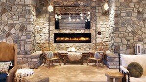 A cozy stone-walled room with a fireplace, two wooden chairs, a sofa, and a small table.