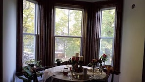 A dining area with a table set for two, large windows with curtains, and potted plants. - Maplehurst Manor B&B (Dorchester)