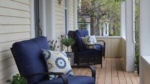 A porch with two blue chairs and patterned cushions, a potted plant, and a view of trees and a house in the background. - Maplehurst Manor B&B (Dorchester)