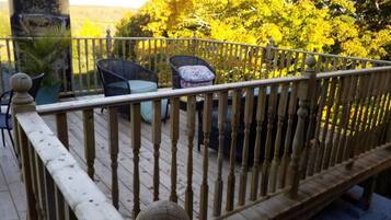A wooden deck with a railing, two wicker chairs, and a potted plant.