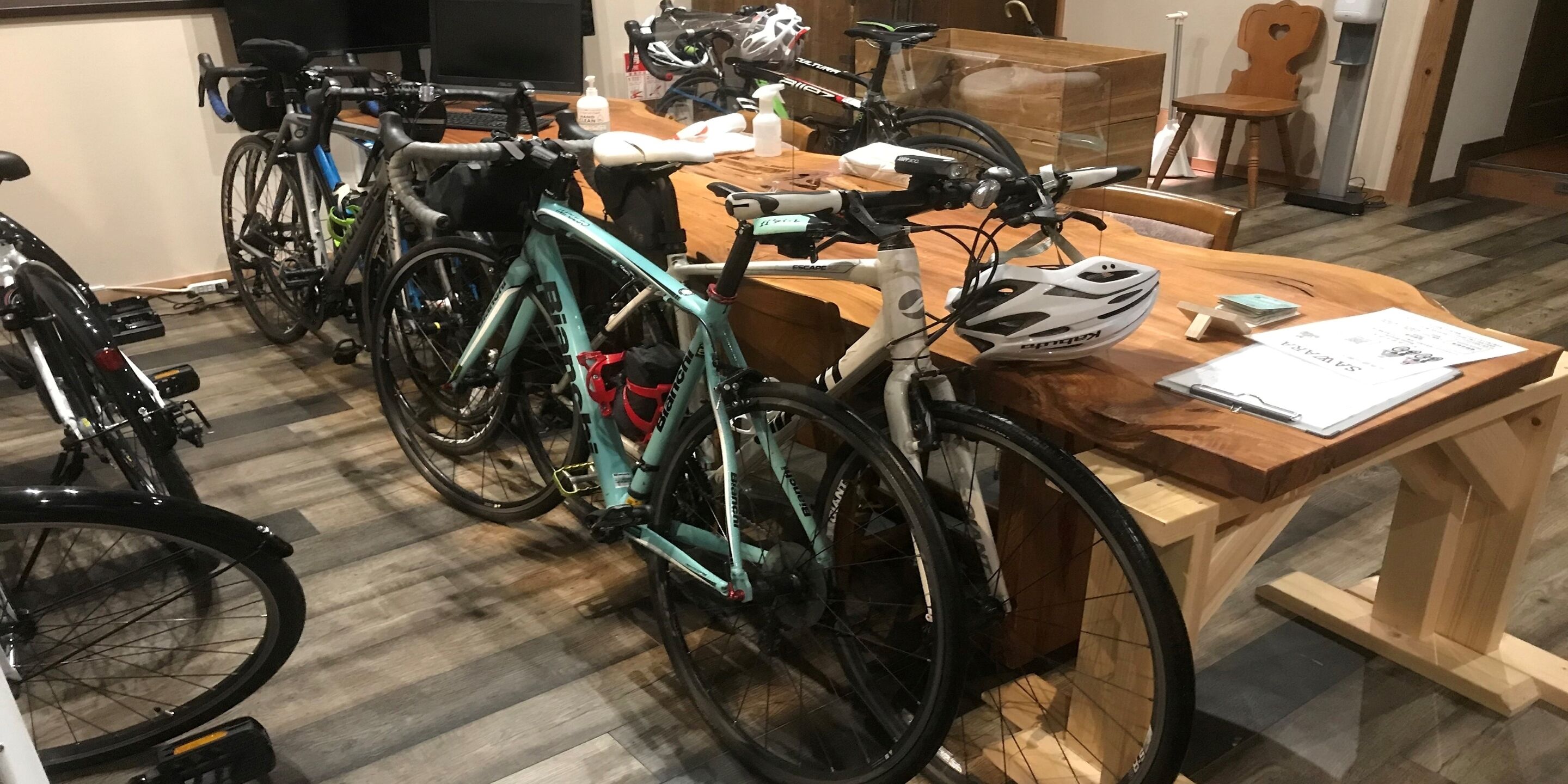 Um quarto com bicicletas encostadas na parede, uma mesa de madeira com papéis e uma cadeira.