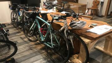Um quarto com bicicletas encostadas na parede, uma mesa de madeira com papéis e uma cadeira.