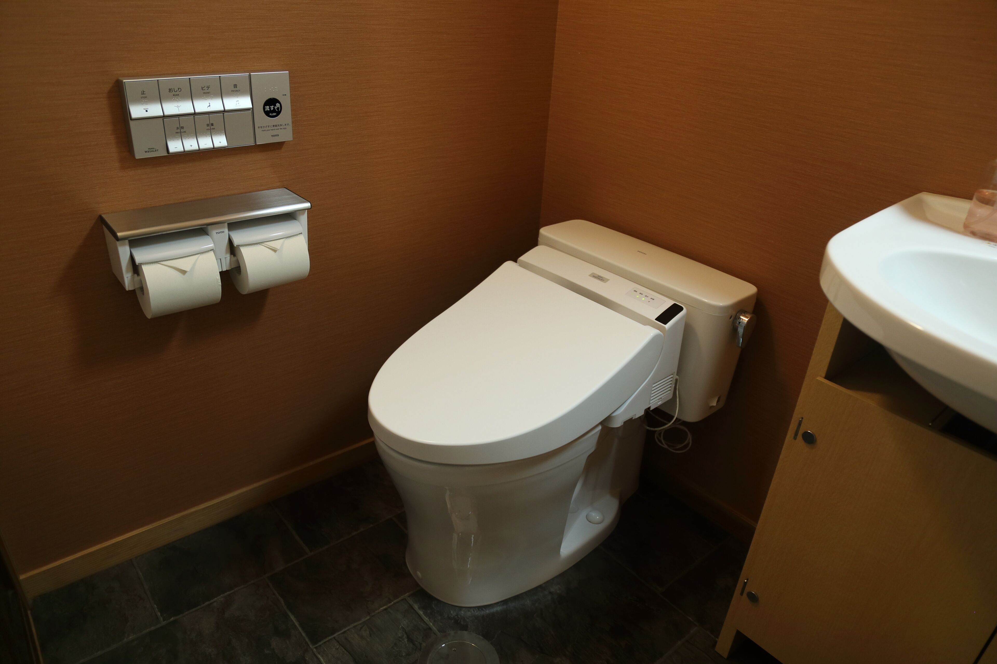 A bathroom with a toilet, a paper towel dispenser, and a sink.
