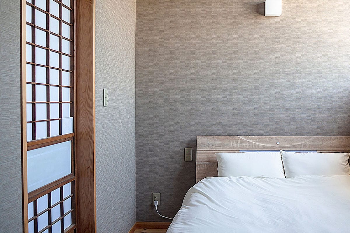A room with a bed, a wooden headboard, a wall-mounted light, and a window with a view.