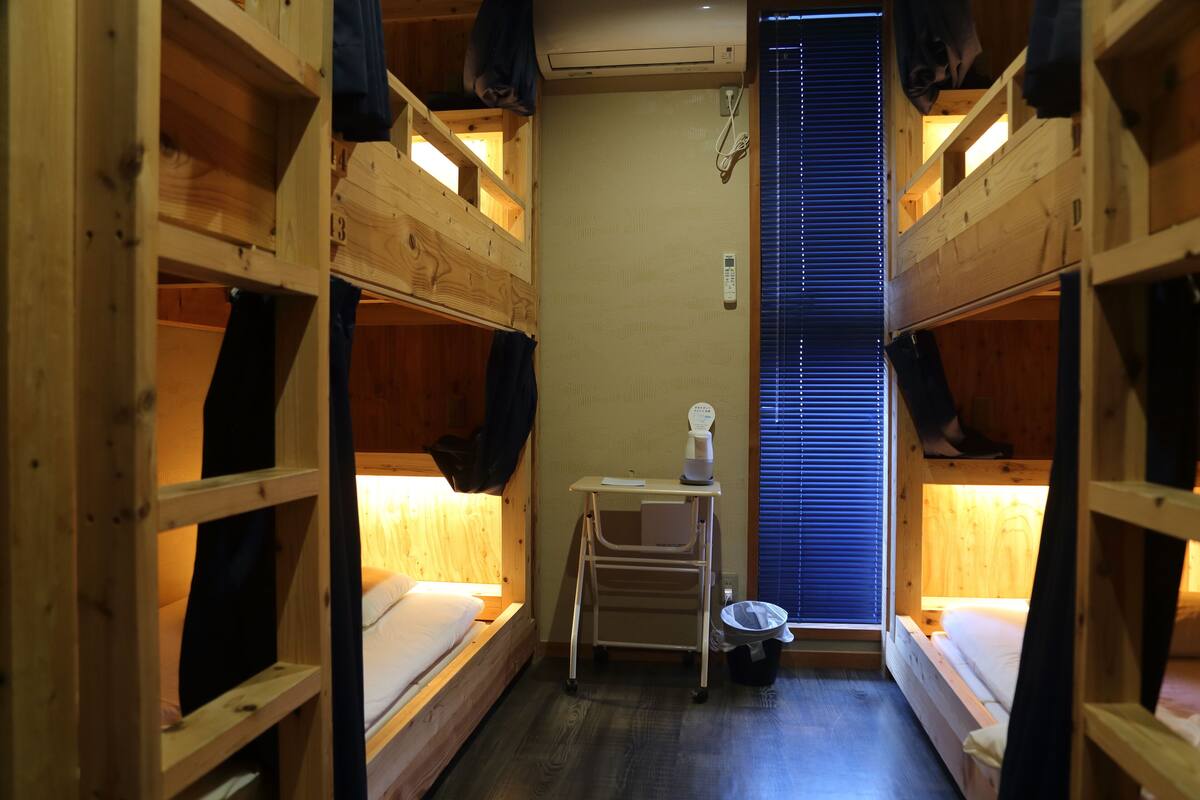 A compact room with bunk beds, a small desk, and a window with blinds.