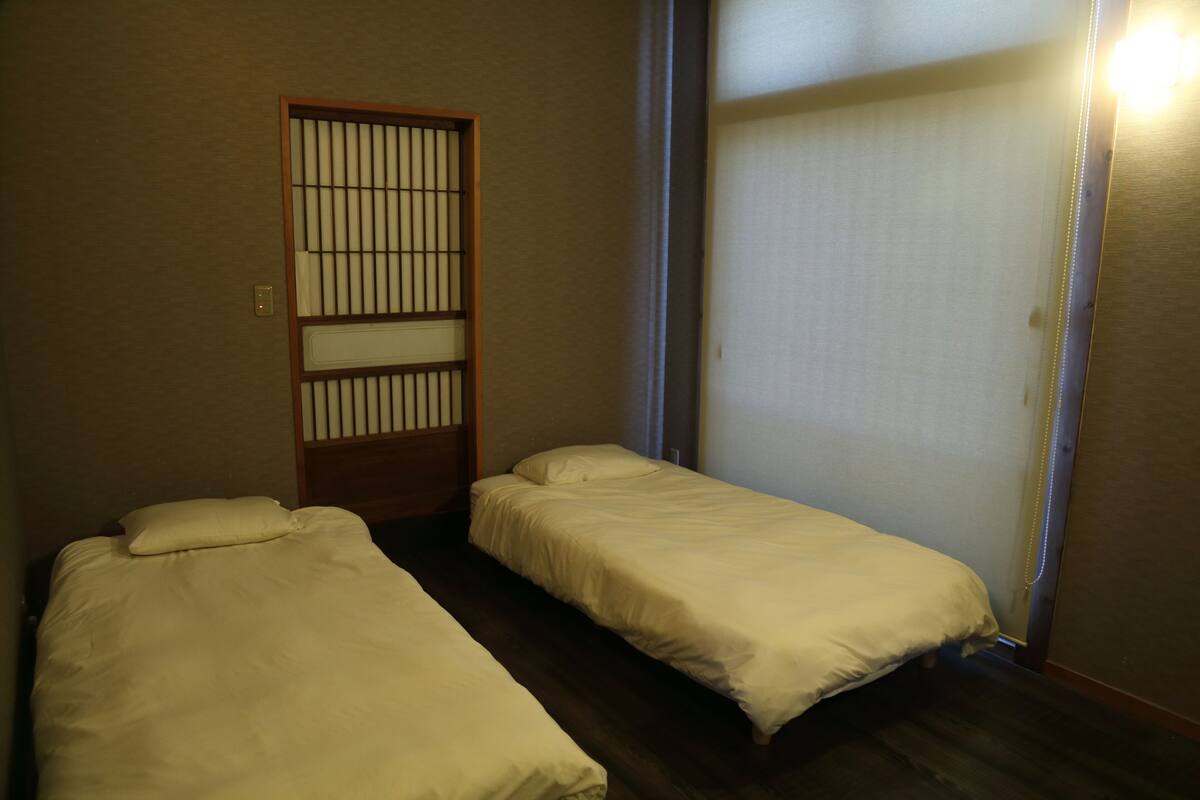 A room with two single beds, a wooden door with vertical slats, and a sliding door with a light fixture.