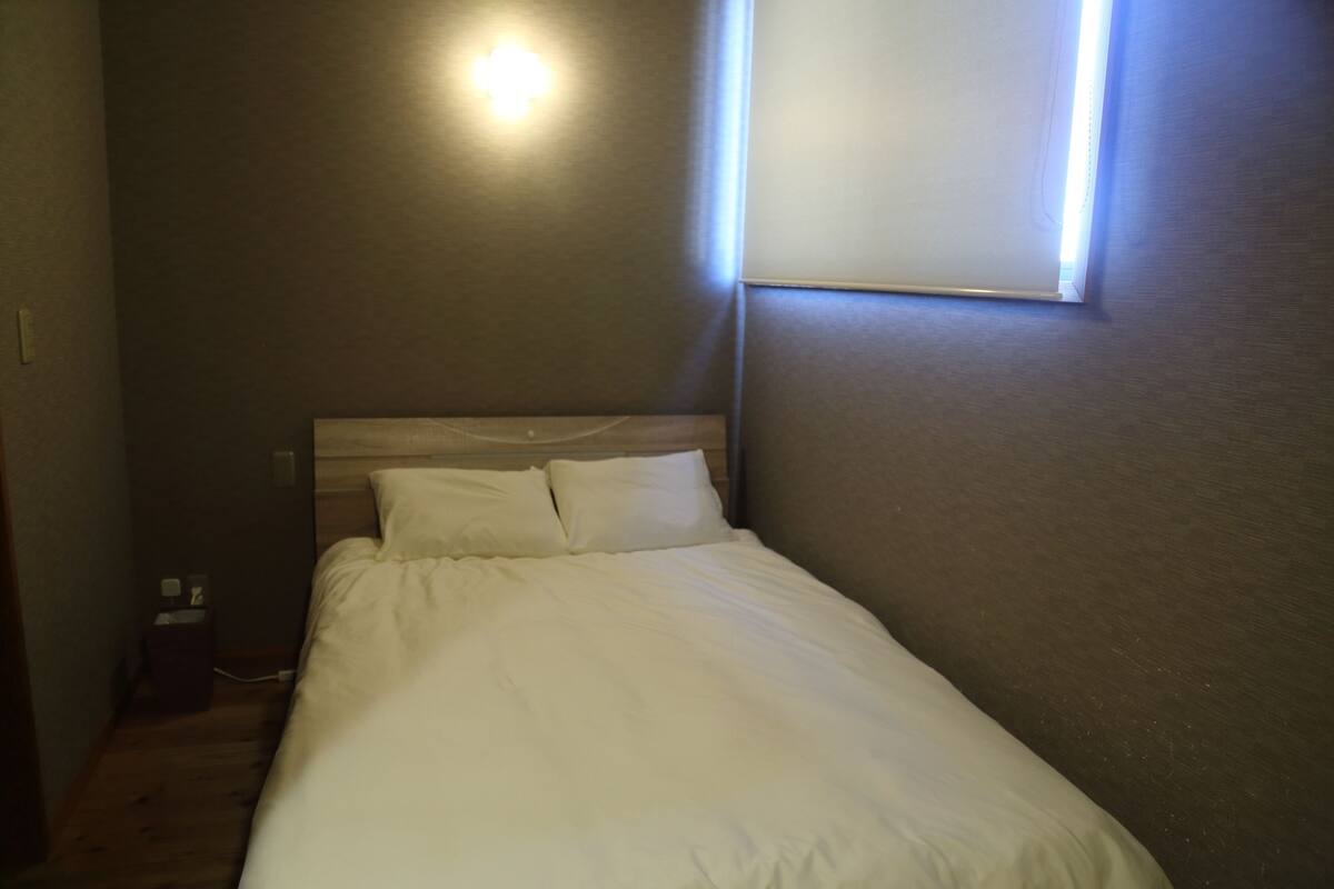 A bedroom with a bed, a nightstand, and a wall-mounted light.