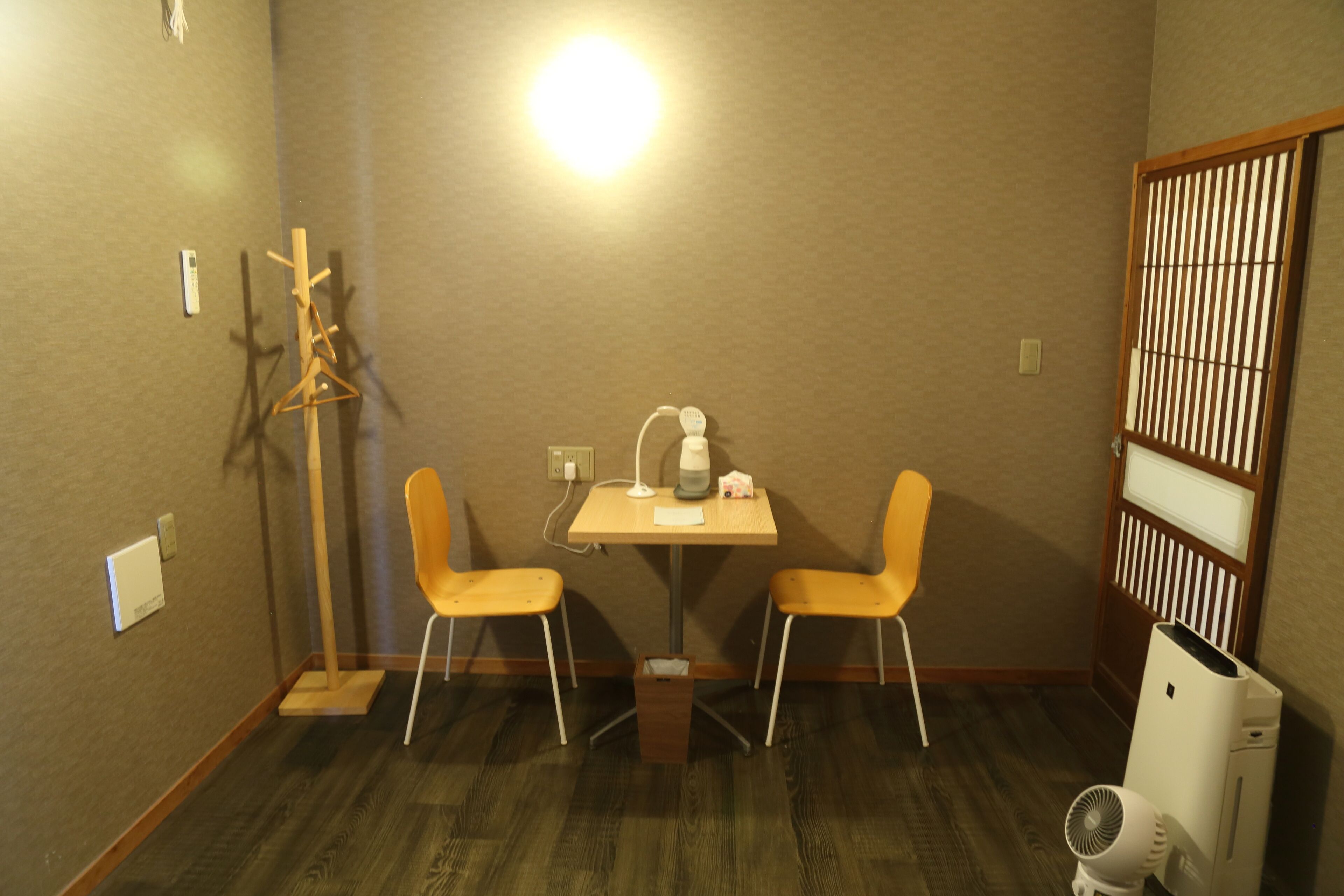 Una habitación pequeña con una mesa de madera, dos sillas, un calentador, un radiador y una partición de madera.