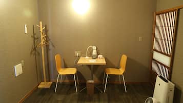 Una habitación pequeña con una mesa de madera, dos sillas, un calentador, un radiador y una partición de madera.