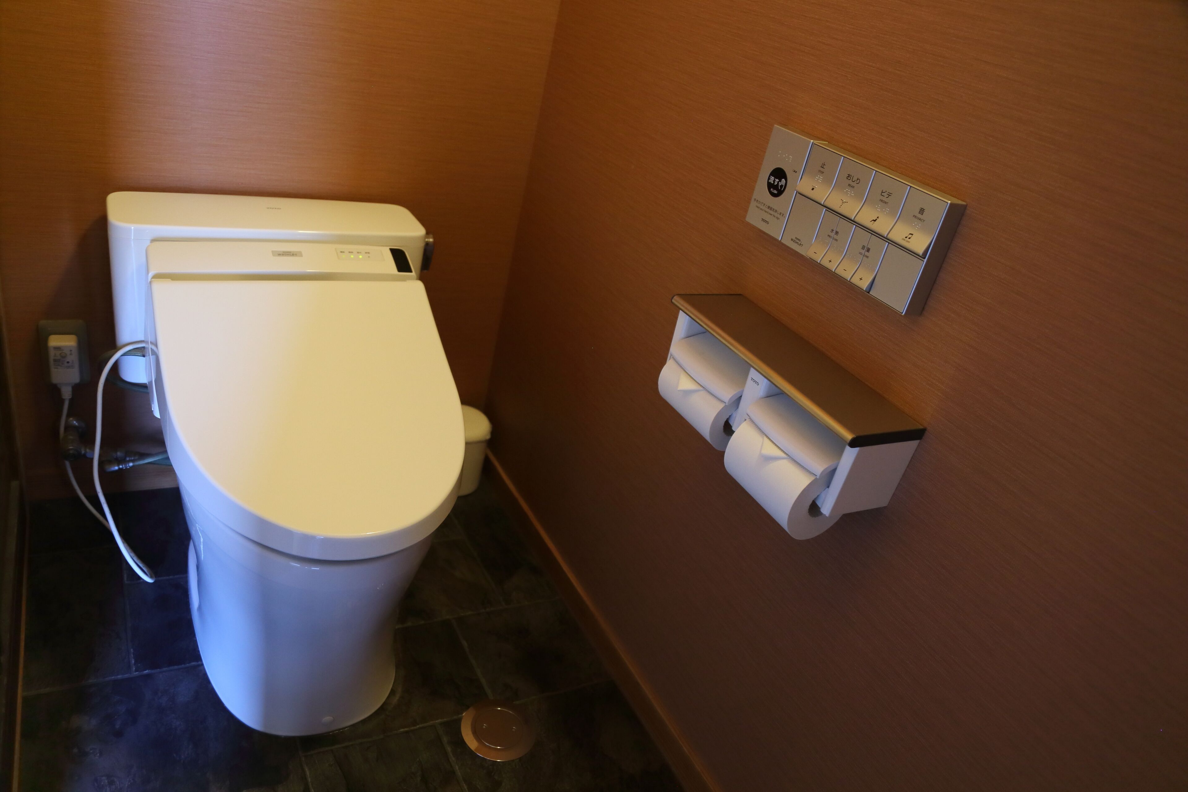 A bathroom with a toilet, a wall-mounted toilet paper holder, and a floor drain.