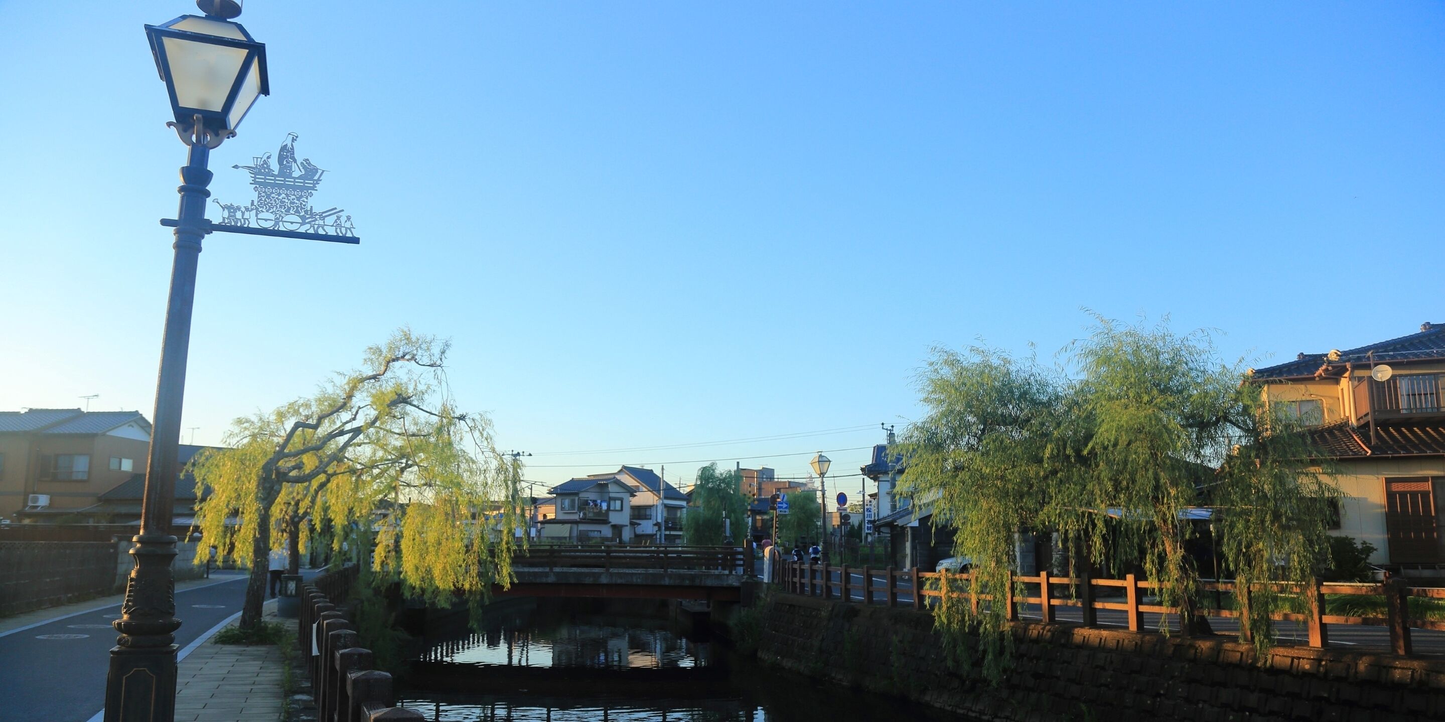 A serene riverside scene with traditional architecture, a bridge, and a lamp post.