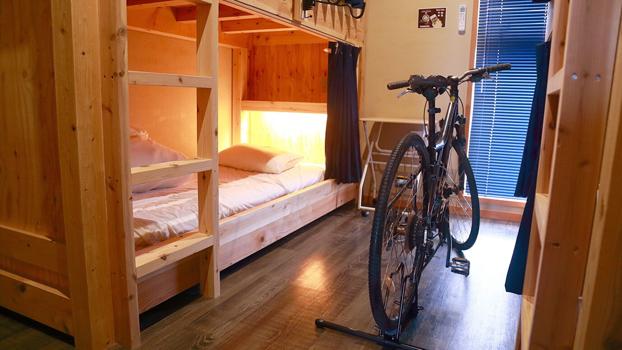 A bunk bed room with a bicycle in the corner, wooden walls, and a window with blinds.
