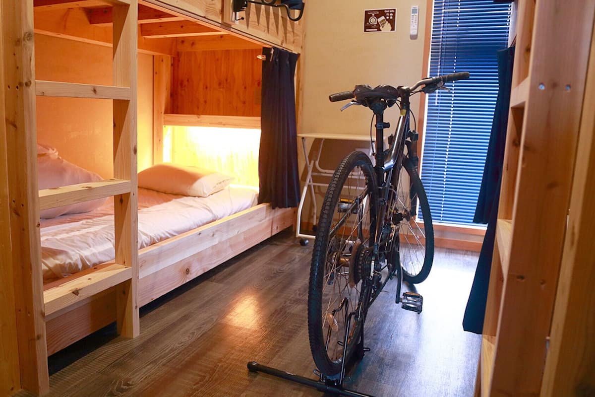 A bunk bed room with a bicycle in the corner, wooden walls, and a window with blinds.