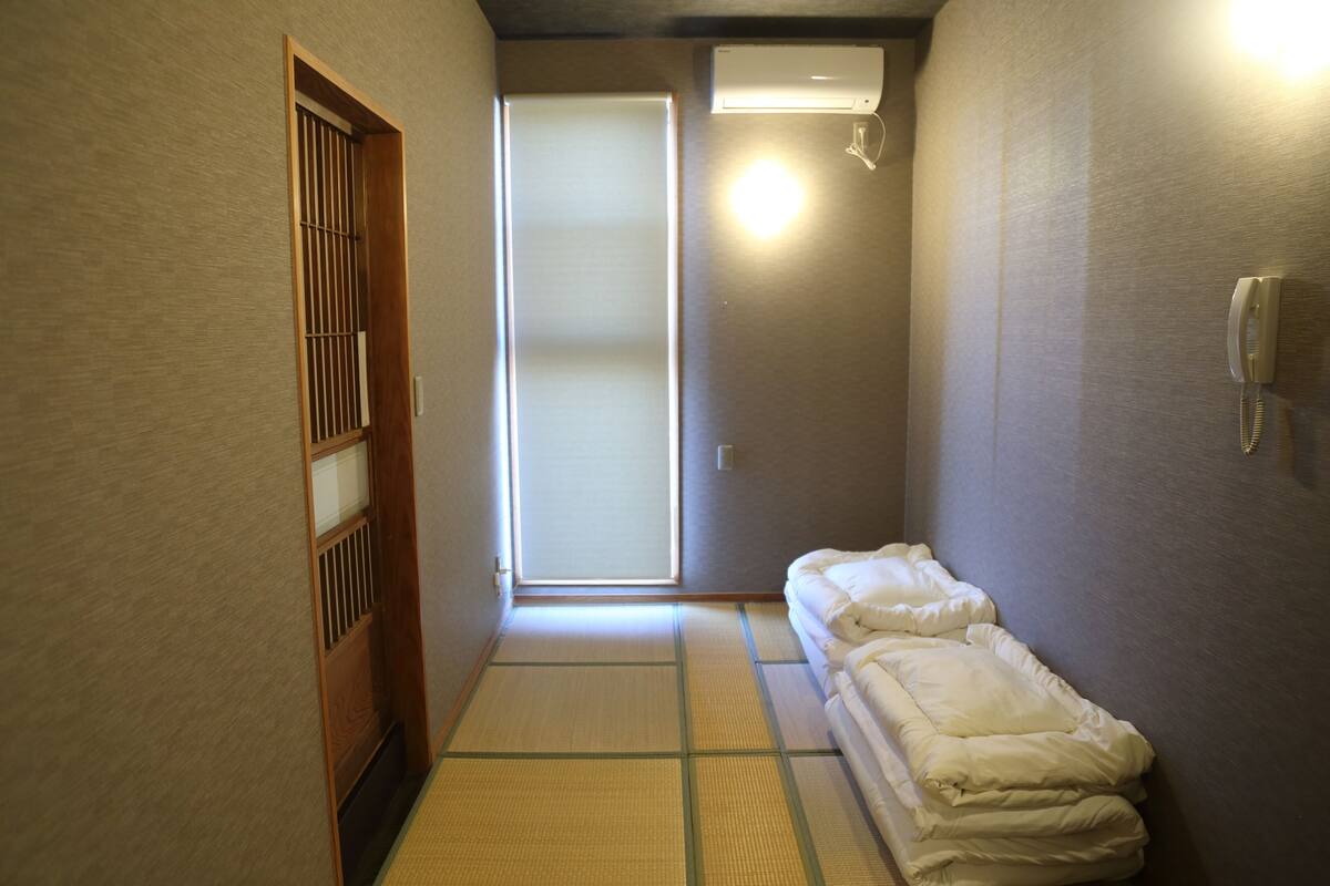 A narrow hallway with tatami mats, a sliding door, and a bed with white bedding.