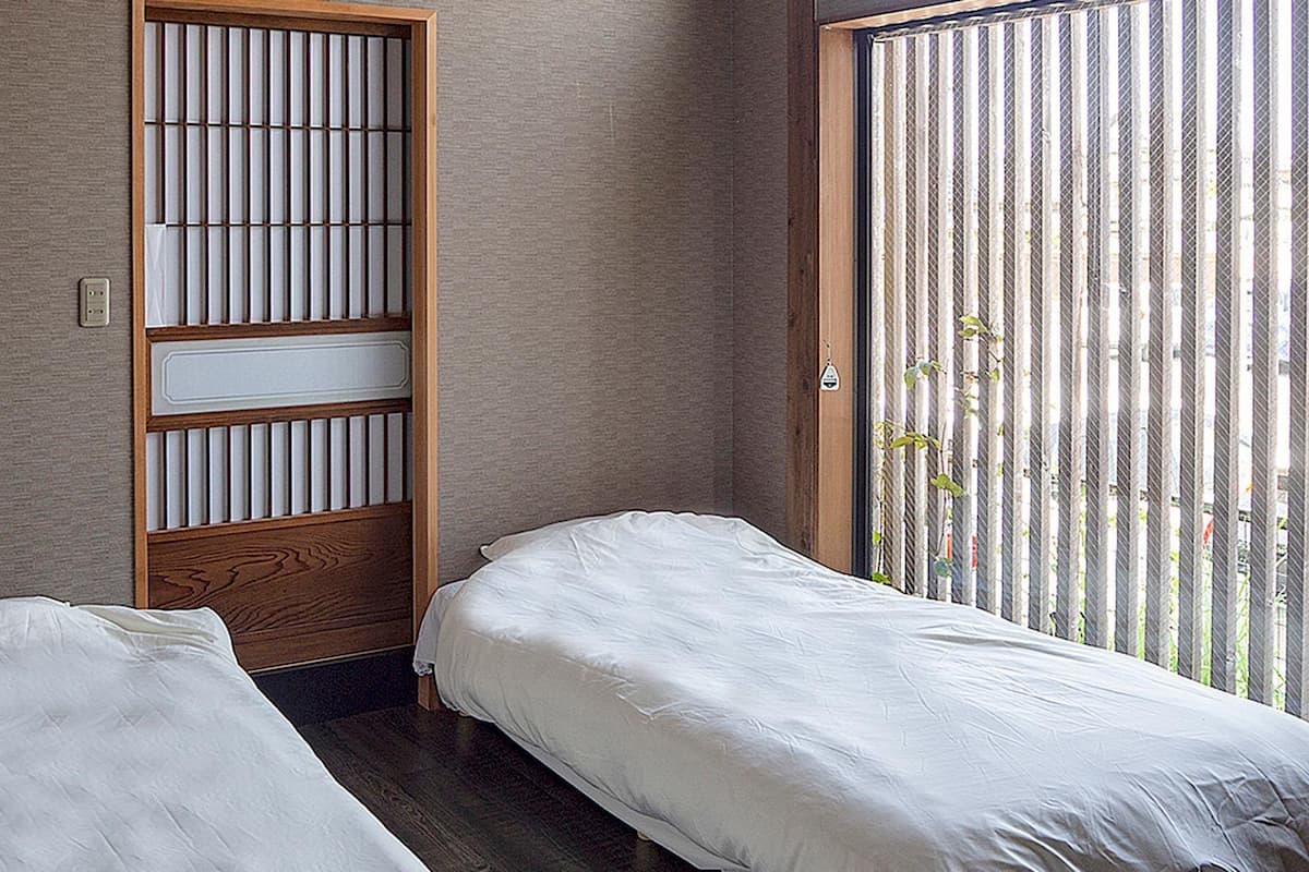 A room with two single beds, a wooden partition with vertical slats, and a window with vertical blinds.