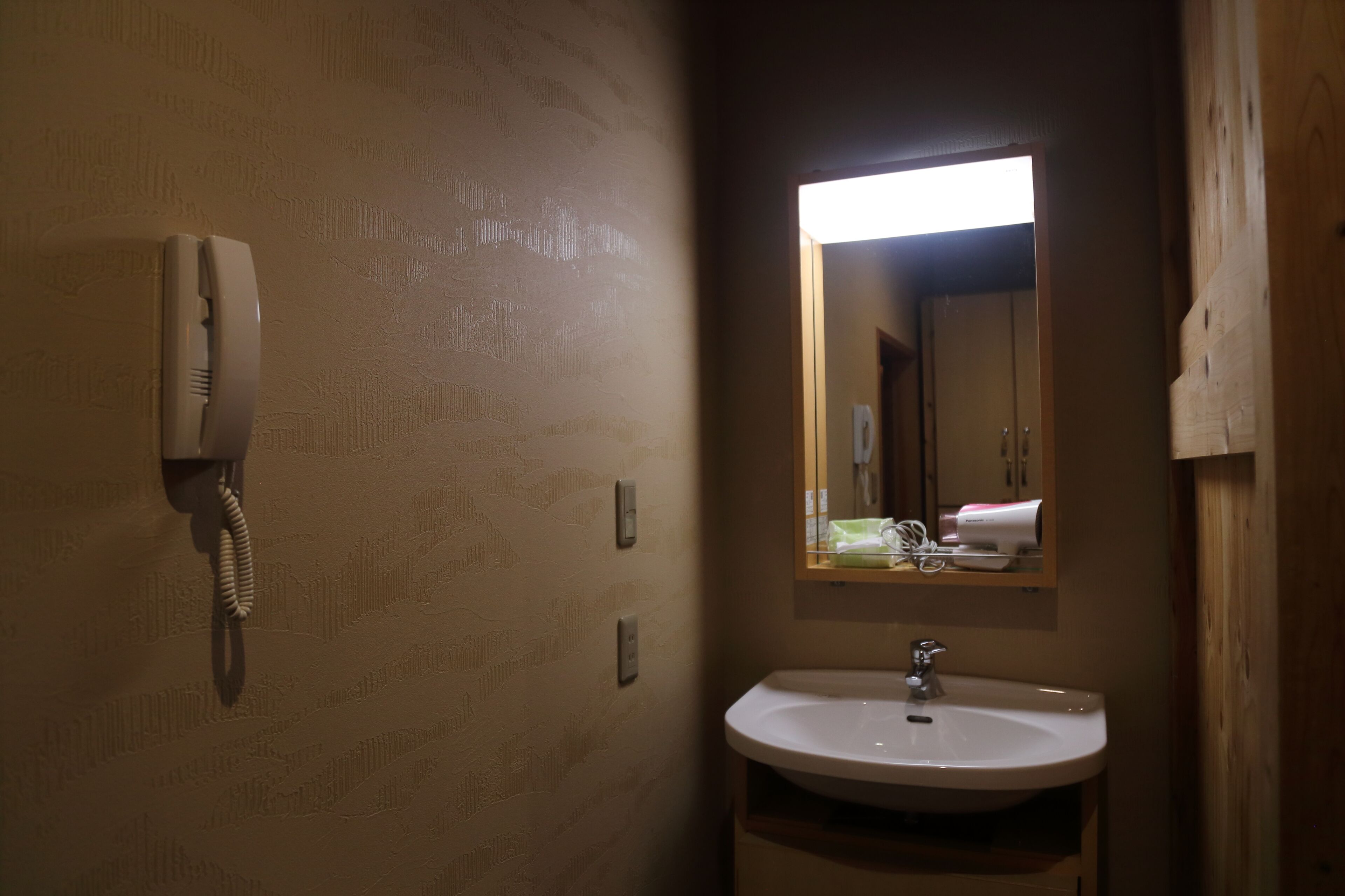 A bathroom with a telephone, a sink, and a mirror.