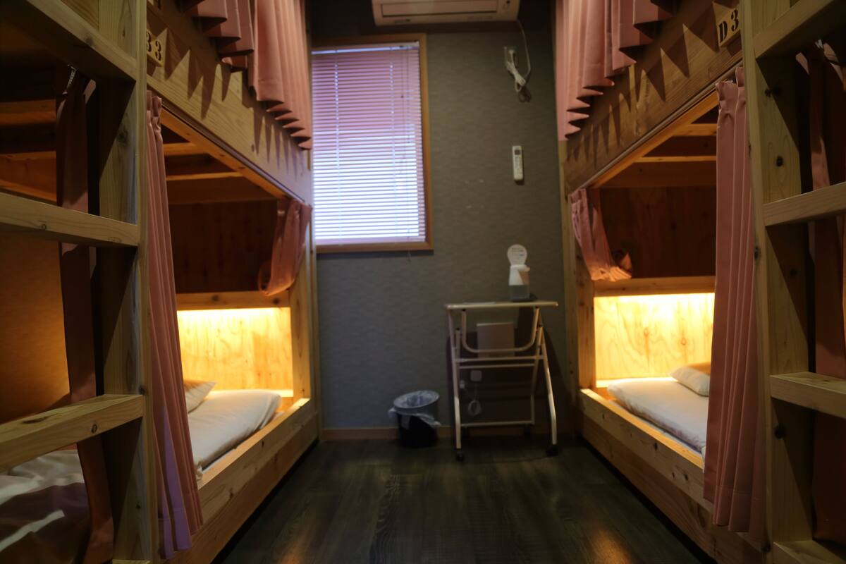 A room with bunk beds, a small desk, and a window with blinds.