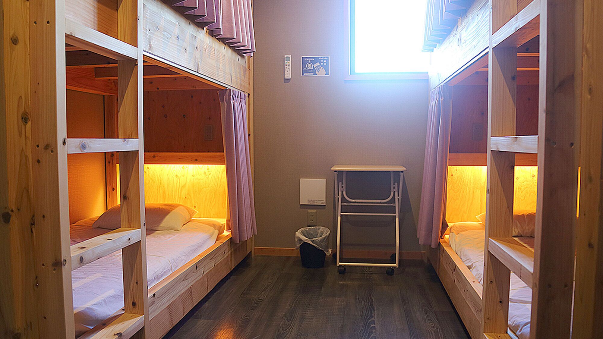 A narrow room with bunk beds, a small table, and a trash bin.