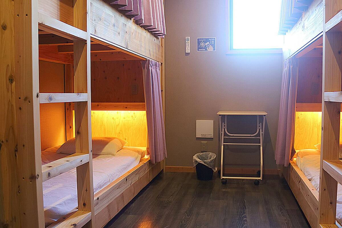 A narrow room with bunk beds, a small table, and a trash bin.