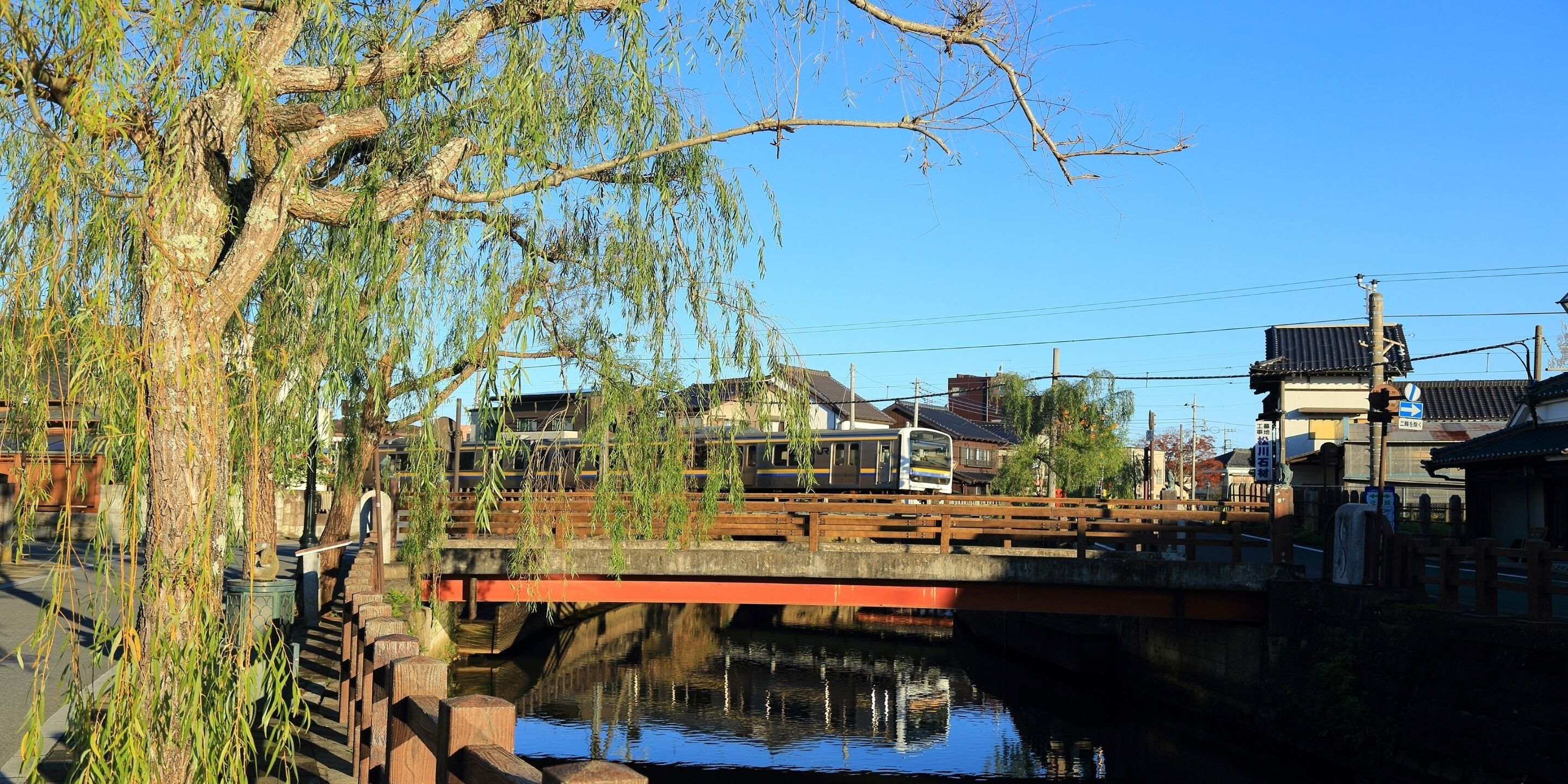 A traditional Japanese bridge over a canal with a train passing underneath.