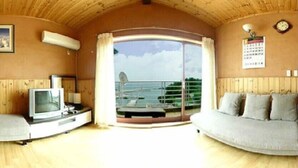 A room with a wooden ceiling, a television, a sofa, and a large window with a view of the sea. - Jisakke Poongyeong Pension (Seogwipo)