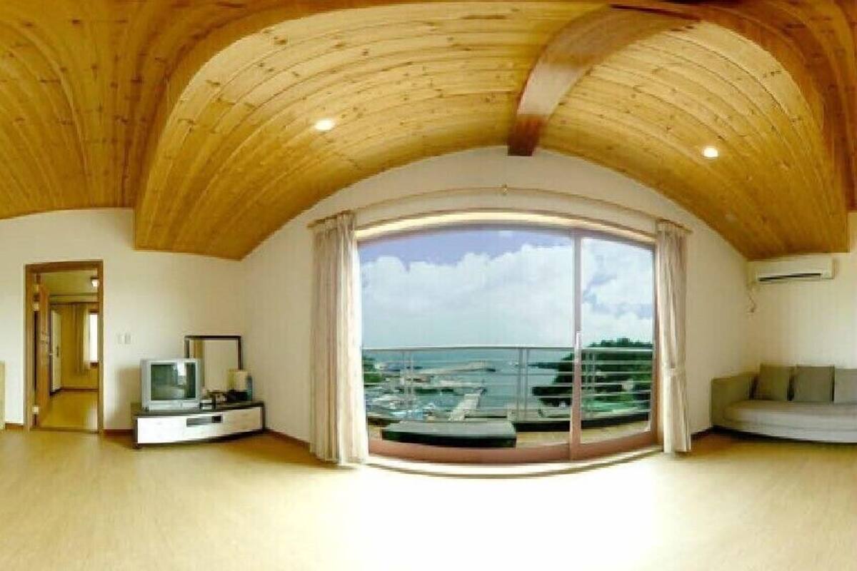A spacious living room with a large sliding glass door leading to a balcony with a view of boats and the sea.