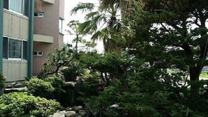 A building with a multi-story structure, surrounded by lush greenery and a small rock garden. - Jisakke Poongyeong Pension (Seogwipo)