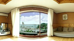 A room with a large sliding glass door leading to a balcony with a view of a marina. There is a sofa and a small table with a television. - Jisakke Poongyeong Pension (Seogwipo)