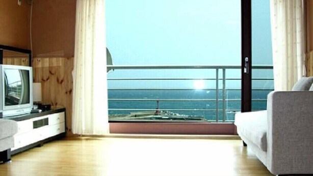 A room with a television, a sofa, and a large window with a view of the sea. - Jisakke Poongyeong Pension (Seogwipo)