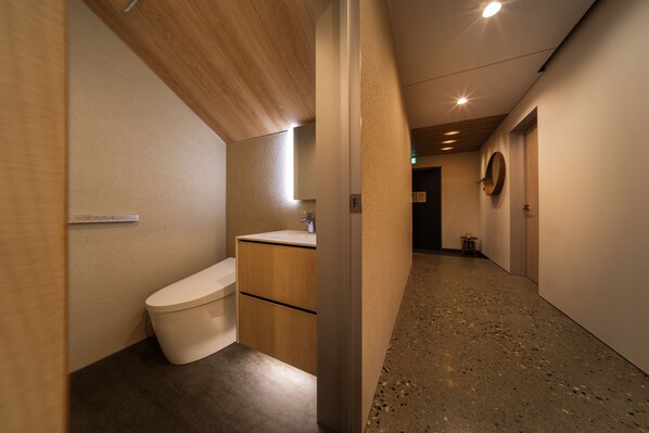 A modern bathroom with a wooden vanity, a toilet, and a sink. - Eminence (Hakuba)