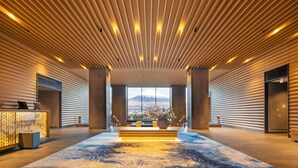 Un vestíbulo moderno con techo de listones de madera, una mesa de recepción, un jarrón grande con flores y vistas a la montaña.