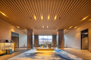 Un vestíbulo moderno con techo de listones de madera, una mesa de recepción, un jarrón grande con flores y vistas a la montaña.