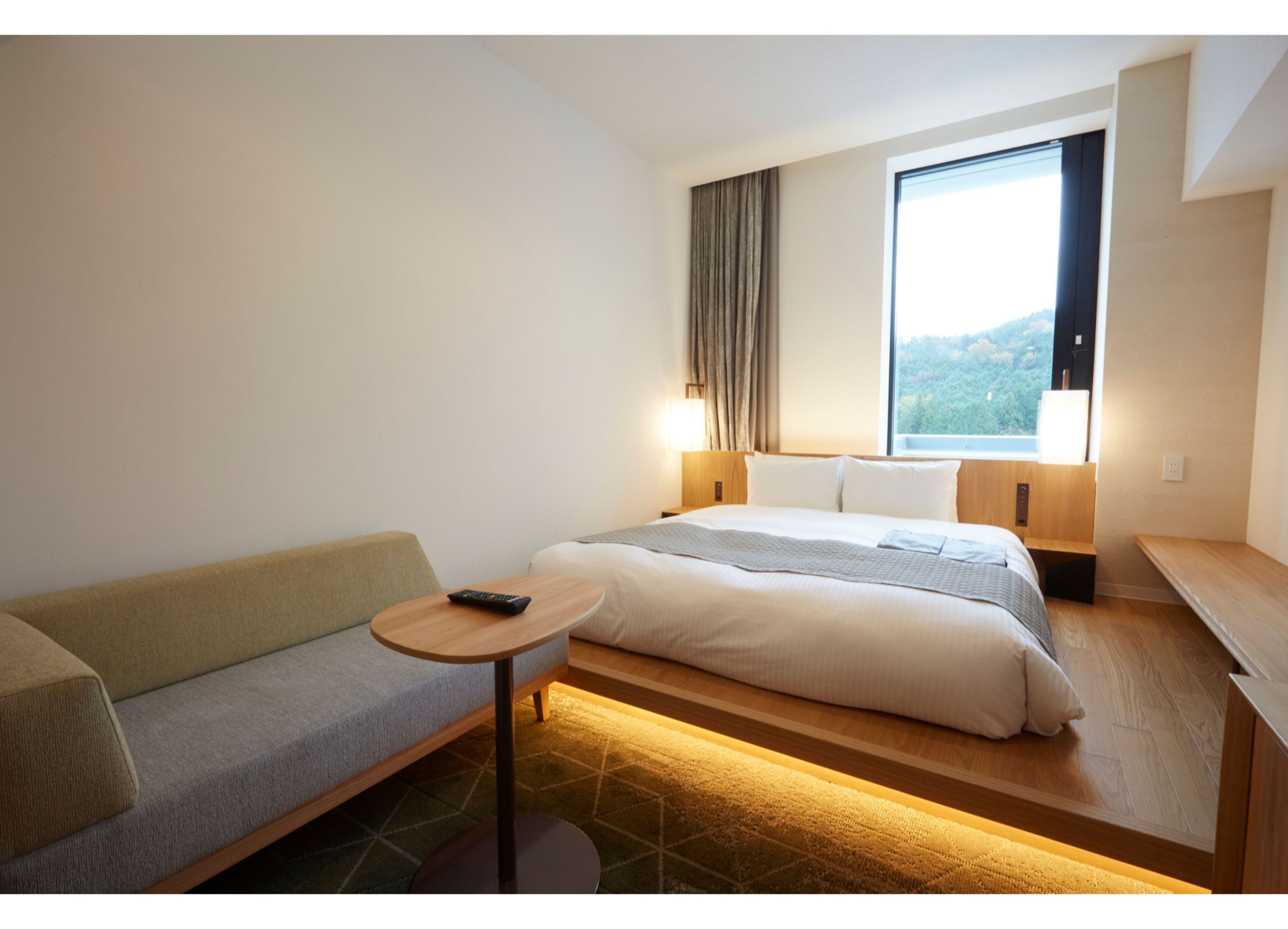 A hotel room with a bed, a sofa, a small table, and a window with a view of the outdoors.