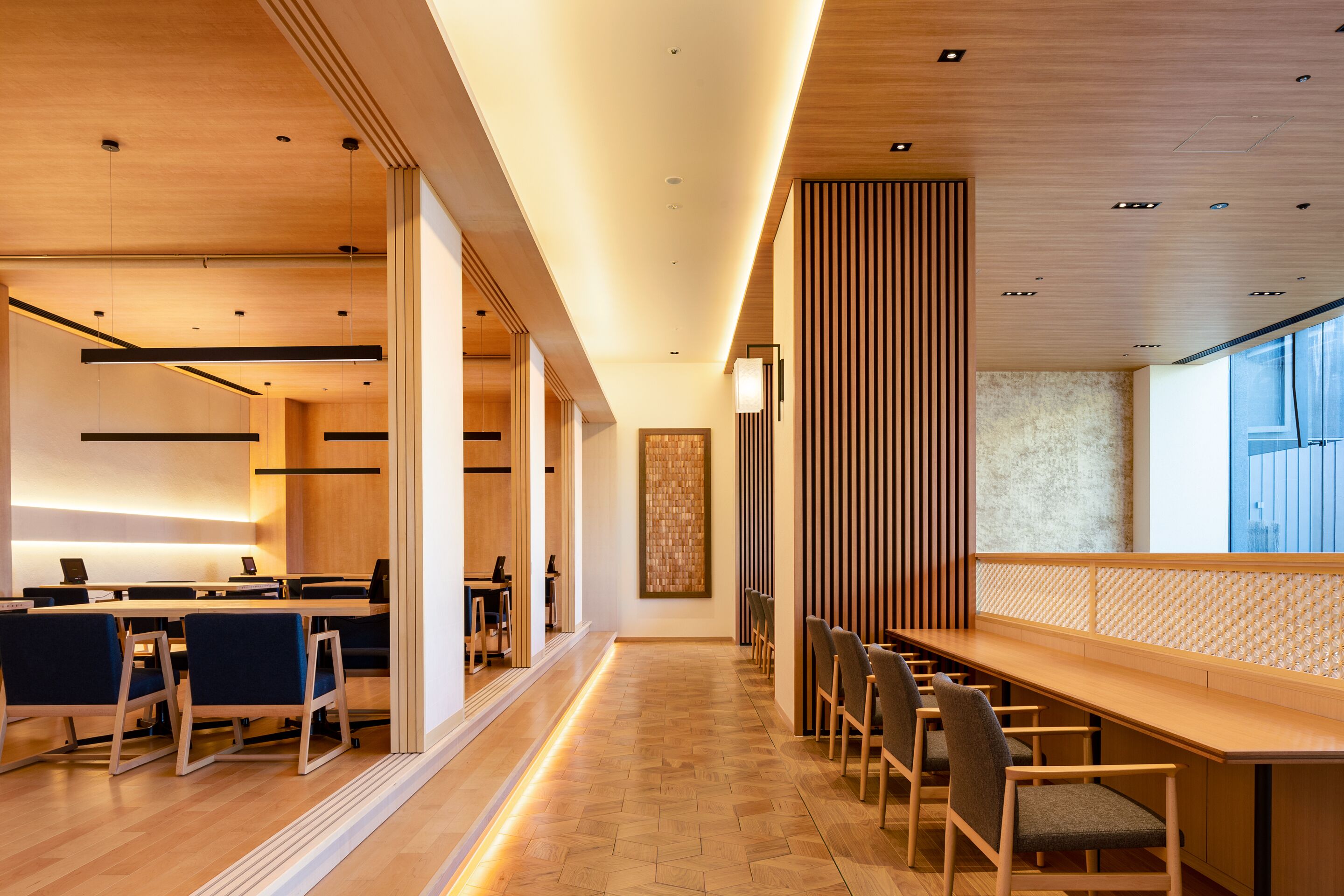 Um hall de hotel moderno com um balcão de recepção extenso, área de estar e uma grande janela que oferece luz natural.