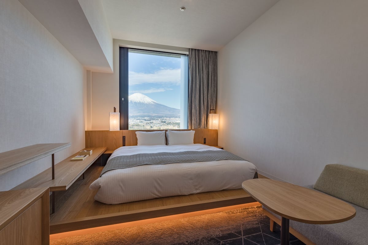 Ein modernes Hotelzimmer mit einem großen Bett, einer Holzbank, einem kleinen Tisch und Blick auf einen Berg.
